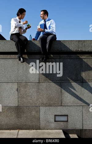 Two businessmen sitting on a wall during a lunch break Stock Photo