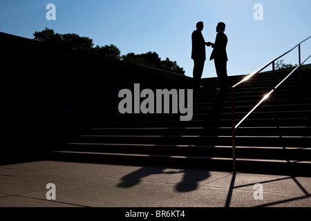 Two businessmen shaking hands, outdoors, silhouette Stock Photo