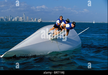 Three crew of a capsized 21 foot Viper one-design keelboat, balancing on the keel in an attempt to right the boat. Stock Photo