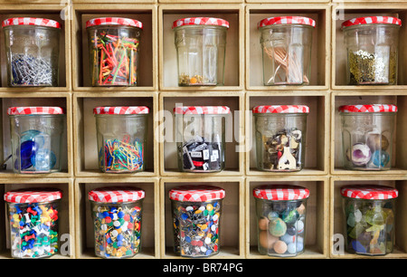 collection of coloured objects stored in old Jam Jars on squared shelf unit. Pins, stones, paper clips, sticks, pebbles, marbles magnetic Words, Stock Photo