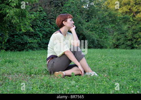 Thoughtful young woman sitting on grass in park Stock Photo