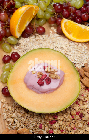 Fresh breakfast with cantaloupe, yogurt and fruit surrounded by healthy condiments of almonds, oats and sunflower seeds. Stock Photo