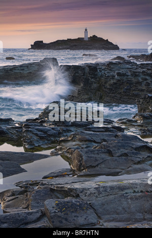View across the rocks to Godrevy Lighthouse Point at sunset with crashing waves St Ives Bay Cornwall UK Stock Photo
