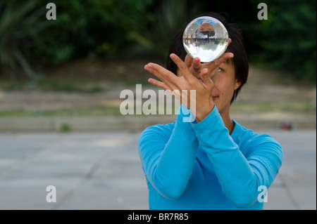 Female Chinese street artist holding and looking into a crystal ball displaying her inverted image Stock Photo