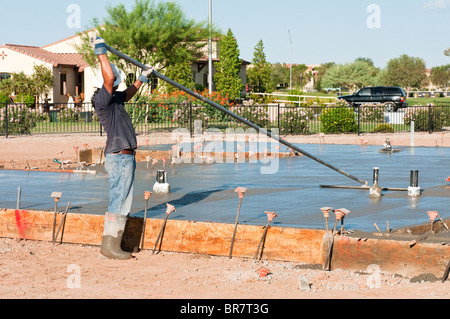 A construction worker finishes a newly poured concrete slab with a float tool. Stock Photo