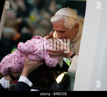 Pope Benedict XVI kisses a baby lifted up to his open car window as he arrives at Hyde Park in his Popemobile. Stock Photo