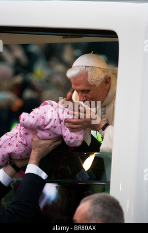 Pope Benedict XVI kisses a baby lifted up to his open car window as he arrives at Hyde Park in his Popemobile. Stock Photo