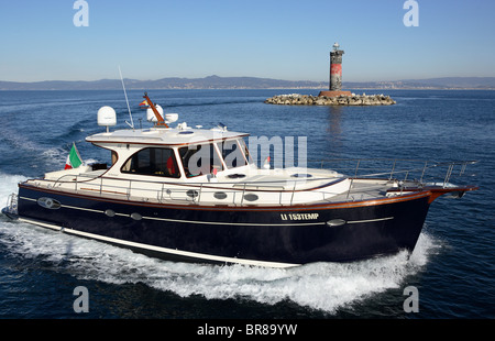 Portland 55 motoryacht, built by Abati yachts, cruising past a lighthouse in the Mediterranean. Tuscany, Italy. Stock Photo