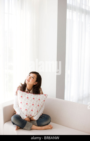 Young woman sitting on sofa, looking up Stock Photo
