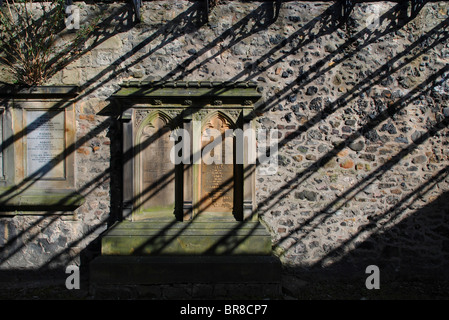 The sun casts shadows of ironwork onto memorials on a wall in South Leith Parish churchyard, Edinburgh, Scotland. Stock Photo