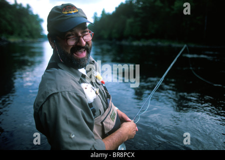 A fly fisherman smiles for the camera while fishing in the east outlet of the Kennebec River near Greenville Maine. Stock Photo