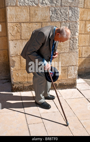 Old hunch-back man with walking stick resting on sidewalk - France. Stock Photo