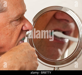 Middle aged / senior man cleaning teeth in front of shaving mirror with electric toothbrush Stock Photo