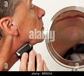 Middle aged man shaving with electric razor in front of shaving mirror Stock Photo