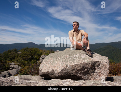 Middle aged hiker on large boulder at the summit of Old Rag in Virginia's Shenandoah valley in the Blue Ridge Mountains, USA Stock Photo