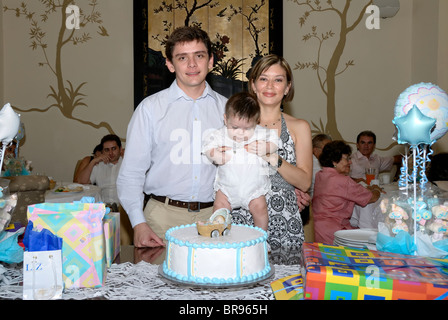 Merida, Yucatan/Mexico-July 8: Baby boy baptism celebration. Father and mother hold their child by the cake and gift table Stock Photo