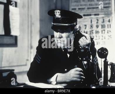 1930s 1940s CONCERNED DETERMINED MAN POLICE SERGEANT IN STATION HOUSE TALKING ON CANDLE STICK TELEPHONE Stock Photo
