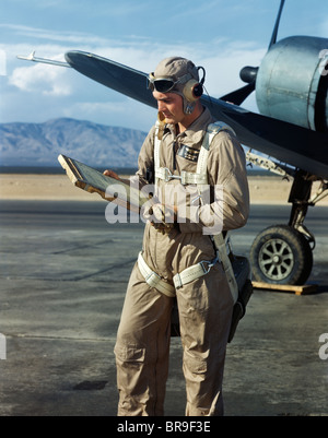 1940s AIR FORCE PILOT STANDING BY PLANE GOING OVER CHECKLIST FLIGHT PLAN WEARING FLYING GOGGLES HELMET COVERALLS AND PARACHUTE Stock Photo