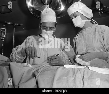 1950s DOCTOR AND NURSE STANDING OVER PATIENT ABOUT TO OPERATE Stock Photo