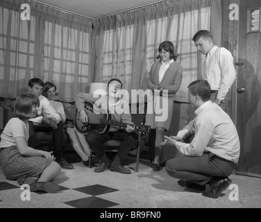 1950s 1960s GROUP OF YOUNG TEENAGERS GATHERING AROUND BOY PLAYING GUITAR Stock Photo