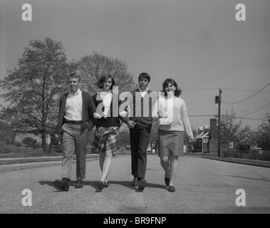 1960s TWO YOUNG TEEN COUPLES WALKING TOGETHER ARM IN ARM LOOKING AT CAMERA Stock Photo