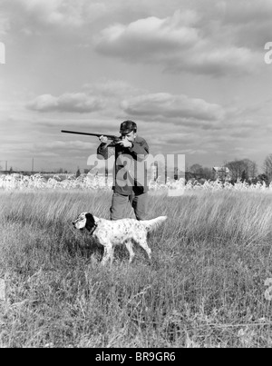 1930s 1940s MAN BIRD HUNTING IN FIELD WITH DOG AIMING SHOTGUN Stock Photo