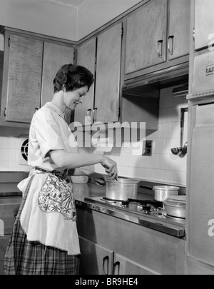 1960s WOMAN KITCHEN COOKING STIRRING POT ON STOVE Stock Photo