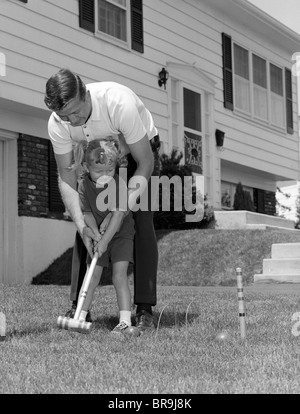 1960s FATHER AND YOUNG DAUGHTER PLAYING CROQUET IN  YARD Stock Photo