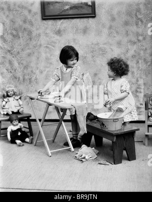 1920s TWO LITTLE GIRLS PLAYING IRONING WASHING DOLL CLOTHES Stock Photo