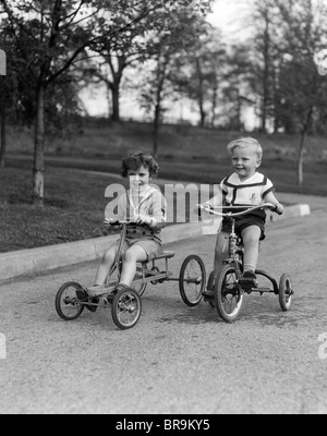 1930s TWO SMILING BOYS RIDING TRICYCLES Stock Photo