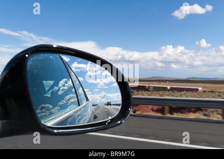 Side view mirror showing cars on the road and clouds reflecting on side of car - suggests moving on from the past Stock Photo