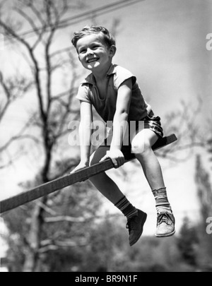 1930s SMILING BOY SITTING ON SEESAW Stock Photo