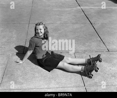 1940s LITTLE GIRL SITTING ON GROUND WEARING ROLLER-SKATES LOOKING AT CAMERA Stock Photo