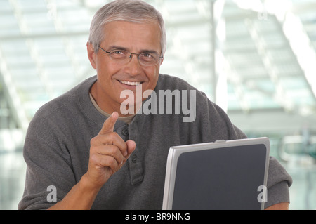Middle aged man sitting at laptop computer and pointing at camera. Stock Photo