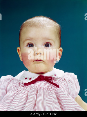 1960s PORTRAIT BABY GIRL SILLY FACIAL EXPRESSION RED BOW AT COLLAR LOOKING AT CAMERA Stock Photo