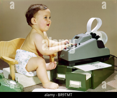 1960s BABY WEARING CLOTH DIAPER SITTING IN BOOSTER CHAIR USING ADDING MACHINE CALCULATOR Stock Photo