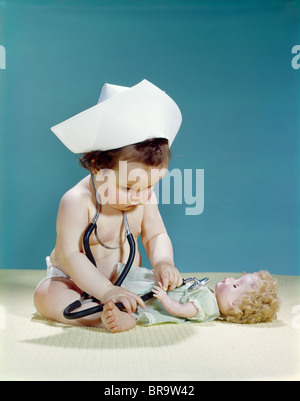 1960s BABY WEARING NURSE NURSE'S CAP STETHOSCOPE LISTENING TO DOLL HEARTBEAT CHEST Stock Photo