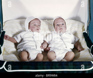 1950s 1960s TWIN BOYS DRESSED IN WHITE LYING IN STROLLER SIDE BY SIDE Stock Photo
