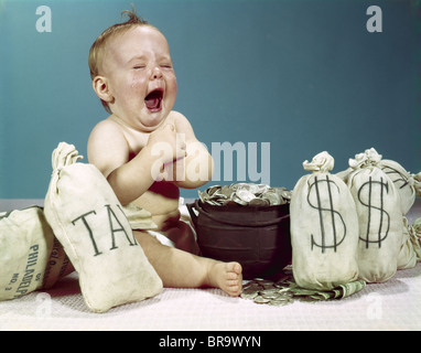 1960s BABY CRYING LAUGHING MOUTH WIDE OPEN WITH POT OF COINS AND BAGS OF MONEY INCLUDING BAG LABELED TAX Stock Photo