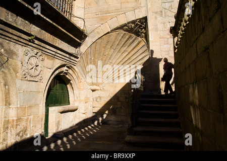 A woman walks down stairs leading out of the Cathedral and past a large scallop shell symbol of Saint James. Stock Photo