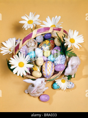 1970s EASTER STILL LIFE OVERHEAD VIEW BASKET FILLED WITH CANDY DECORATED EGGS DAISIES BUNNY FIGURINES Stock Photo