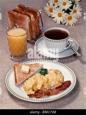 1960s 1970s SCRAMBLED EGGS BACON TOAST ON DISH GLASS ORANGE JUICE TOAST IN RACK CUP OF COFFEE DAISIES BREAKFAST Stock Photo