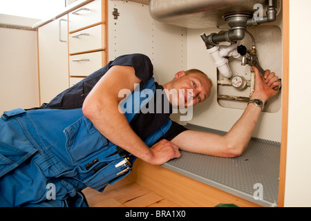 Heating and sanitary technician repairing the leaky pipes under the kitchen sink Stock Photo