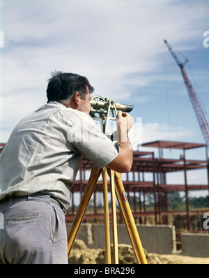 1960s MAN USING SURVEYING EQUIPMENT SIGHTING SURVEYOR TRANSIT THEODOLITE ENGINEER CONSTRUCTION SITE RETRO Stock Photo