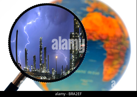 Lightning during thunderstorm above petrochemical industry seen through magnifying glass held against terrestrial globe Stock Photo