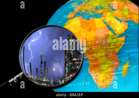 Lightning during thunderstorm above petrochemical industry seen through magnifying glass held against terrestrial globe Stock Photo