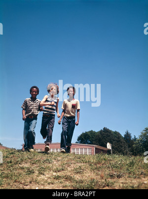 1970 1970s TWO AFRICAN AMERICAN ONE WHITE BOY WALKING ACROSS GRASS Stock Photo