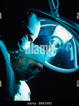 1970s TWO DOCTORS UNDER OPERATING ROOM LIGHT WEARING SURGEONS MASK AND SCRUBS Stock Photo
