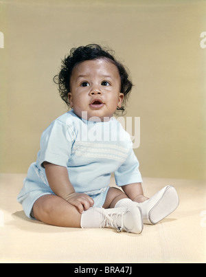 1960s PORTRAIT AFRICAN-AMERICAN BABY BOY WEARING BLUE OUTFIT WHITE SHOES LOOKING TO SIDE Stock Photo