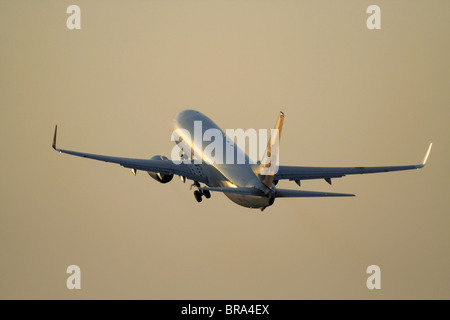 Air travel. Boeing 737 NG passenger jet plane taking off at sunset on flight path in an orange sky. View from behind with proprietary details deleted. Stock Photo